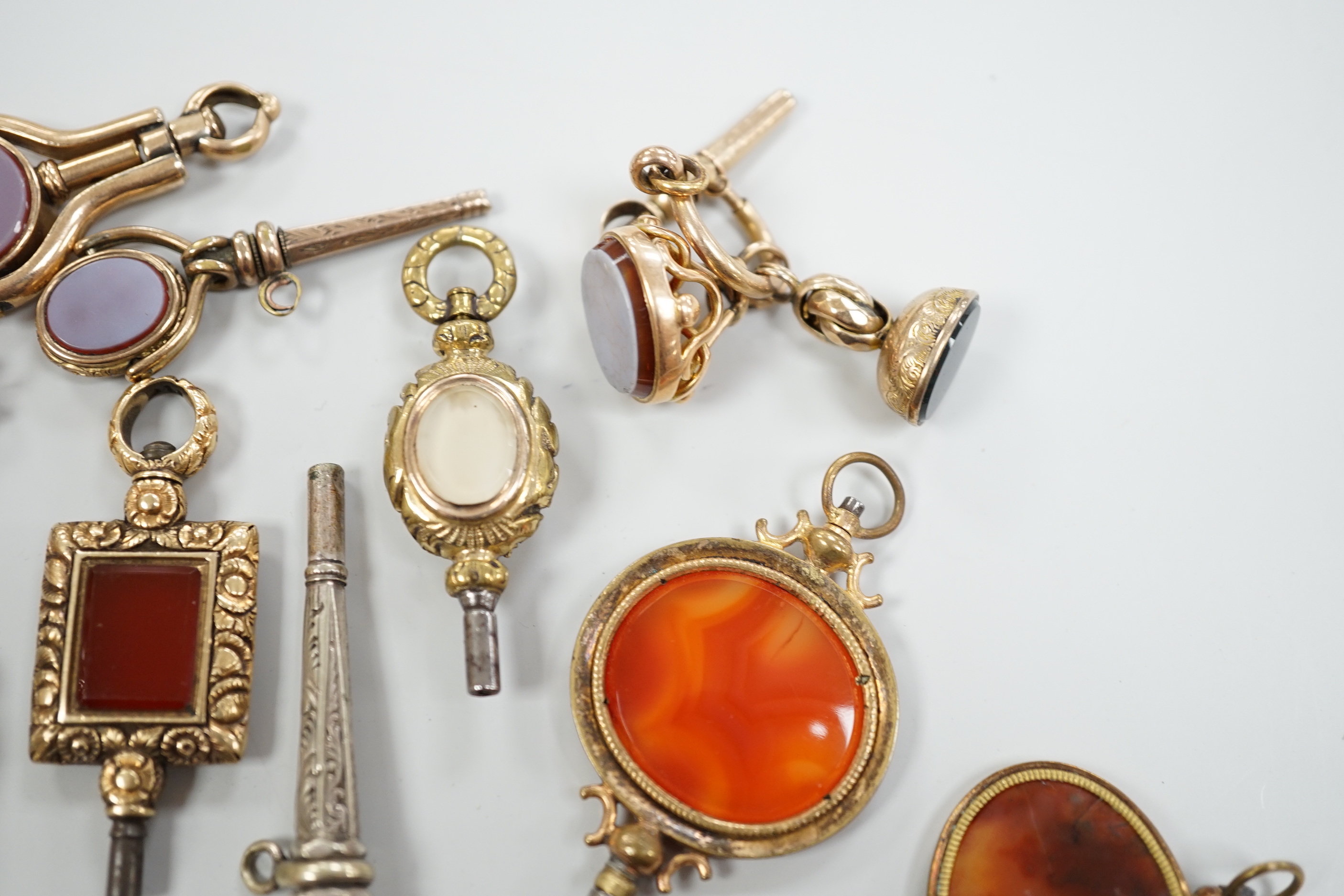 Sixteen assorted 19th century and later, 9ct gold and yellow or white metal overlaid and chalcedony set watch keys, including bloodstone, sardonyx, banded agate and moss agate and spinning fobs, largest 56mm.